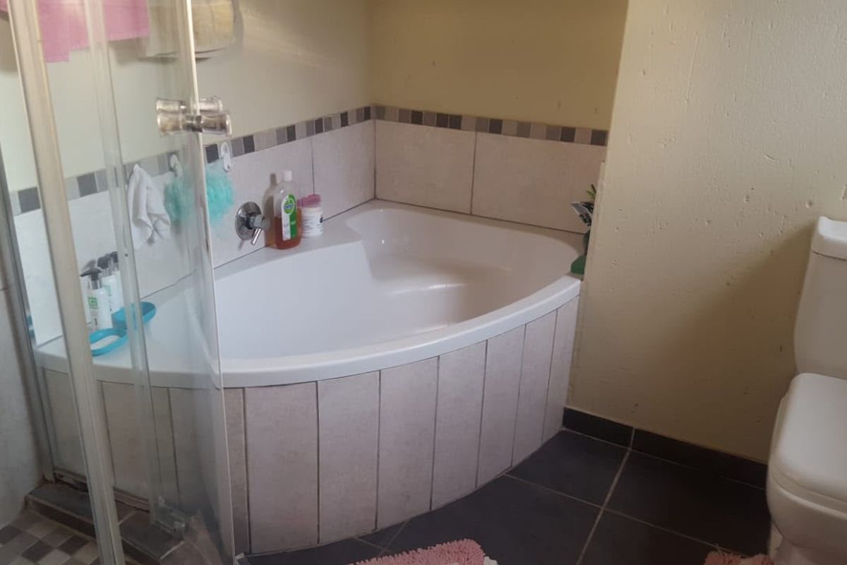 A functional bathroom featuring a corner bathtub, glass shower enclosure, and standard toilet with tiled finishes.