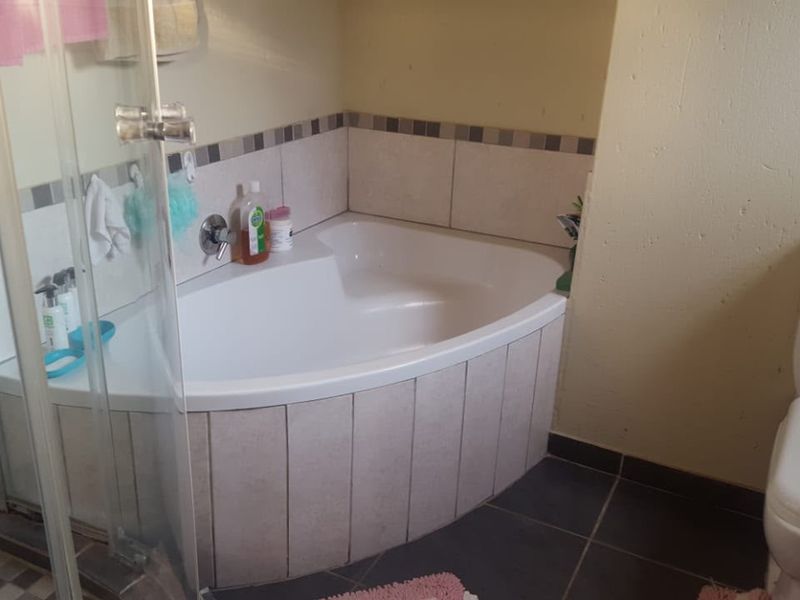 A functional bathroom featuring a corner bathtub, glass shower enclosure, and standard toilet with tiled finishes.