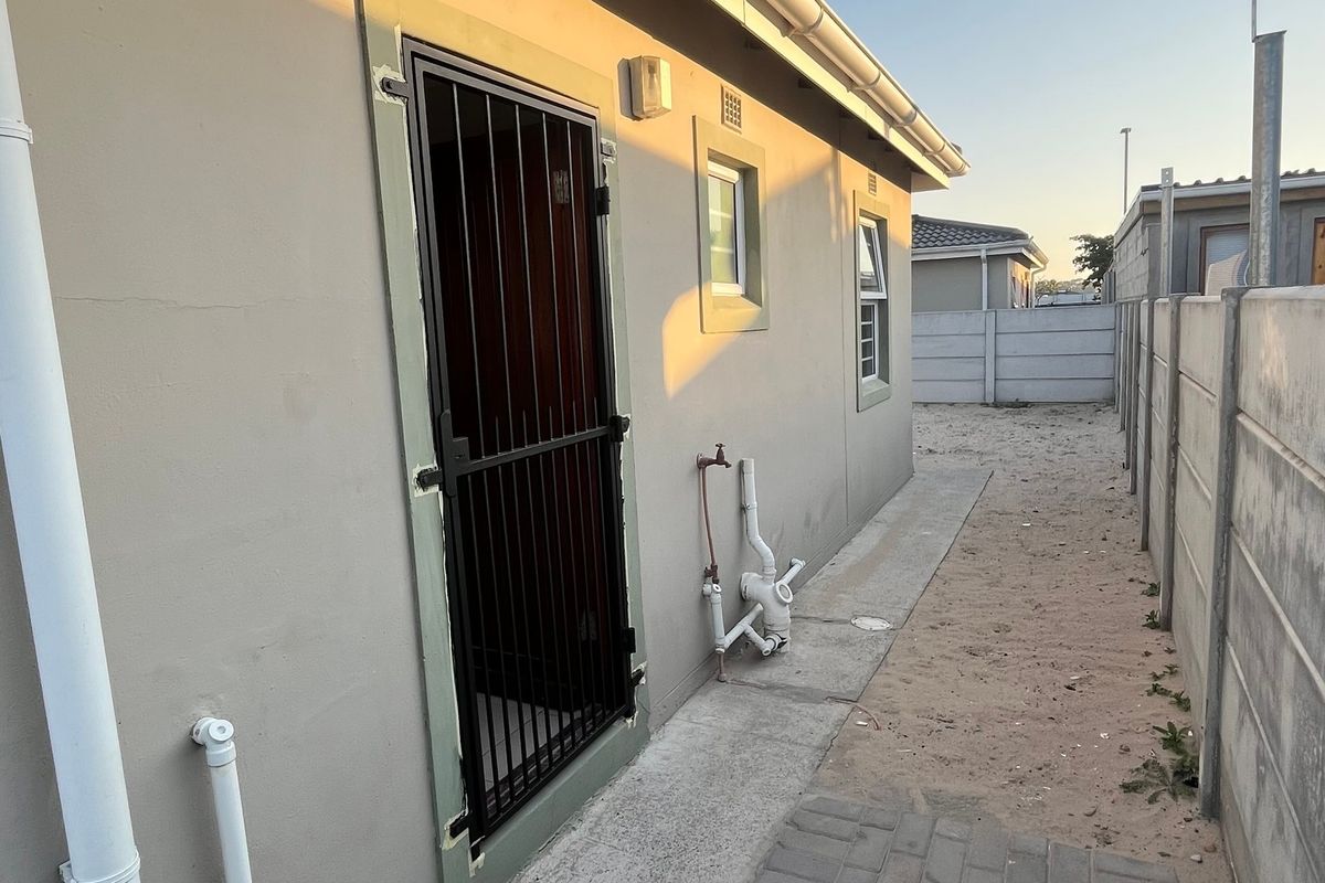 Rear exterior view of the property showing a security gate, external plumbing fixtures, and a precast concrete boundary wall.