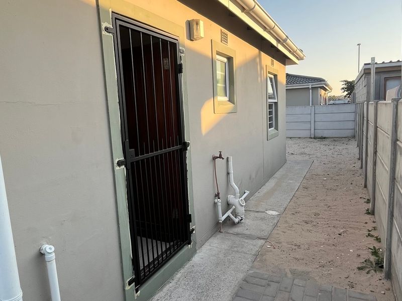 Rear exterior view of the property showing a security gate, external plumbing fixtures, and a precast concrete boundary wall.