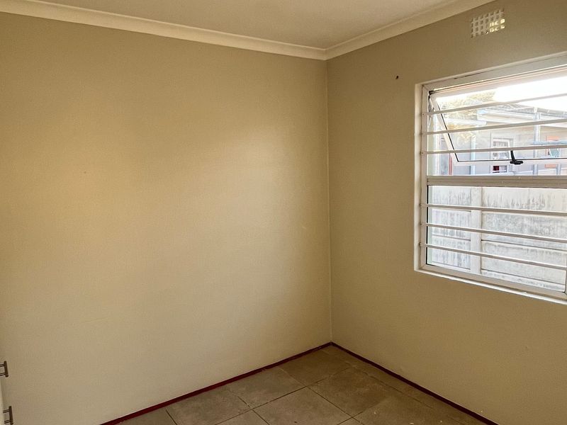 An empty bedroom featuring tiled flooring, a built-in wardrobe, and a louver window with security bars.