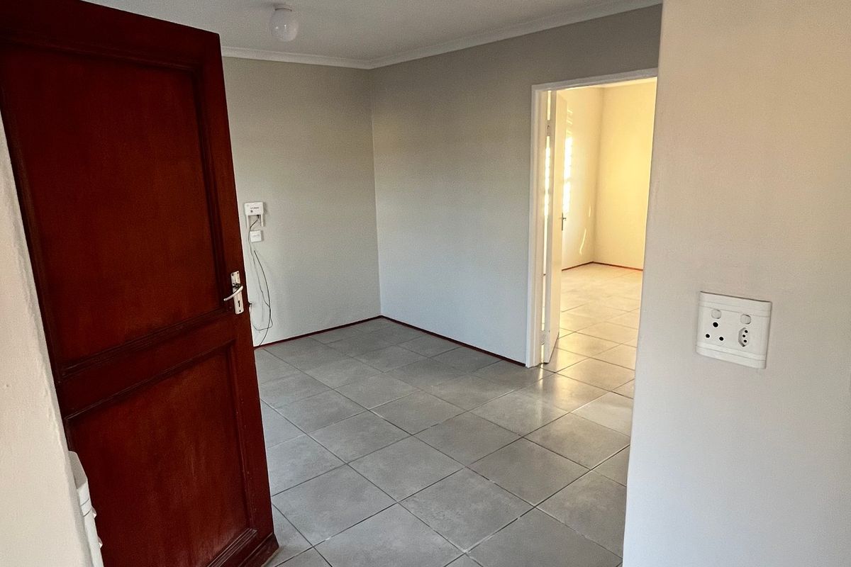 An empty bedroom featuring neutral wall paint, tiled flooring, and a wooden door, providing a clean and versatile space ready for personalization.