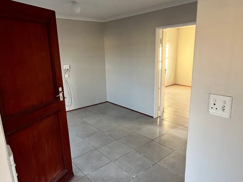 An empty bedroom featuring neutral wall paint, tiled flooring, and a wooden door, providing a clean and versatile space ready for personalization.