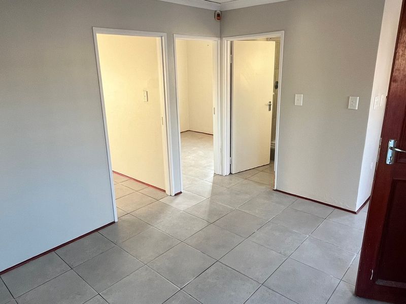 A clean, empty hallway featuring neutral wall paint and light-colored floor tiles, providing access to multiple rooms within the home.