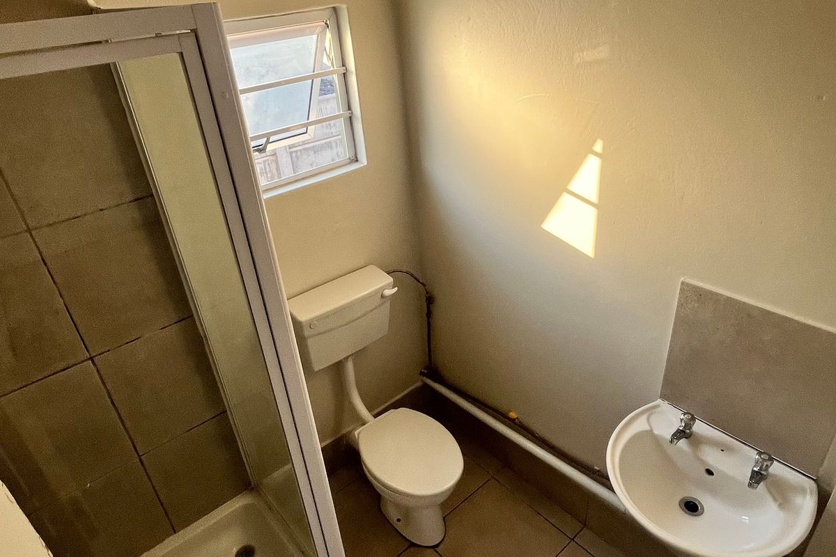 A functional bathroom featuring a shower enclosure, toilet, and wall-mounted basin with tiled flooring and neutral wall finishes.