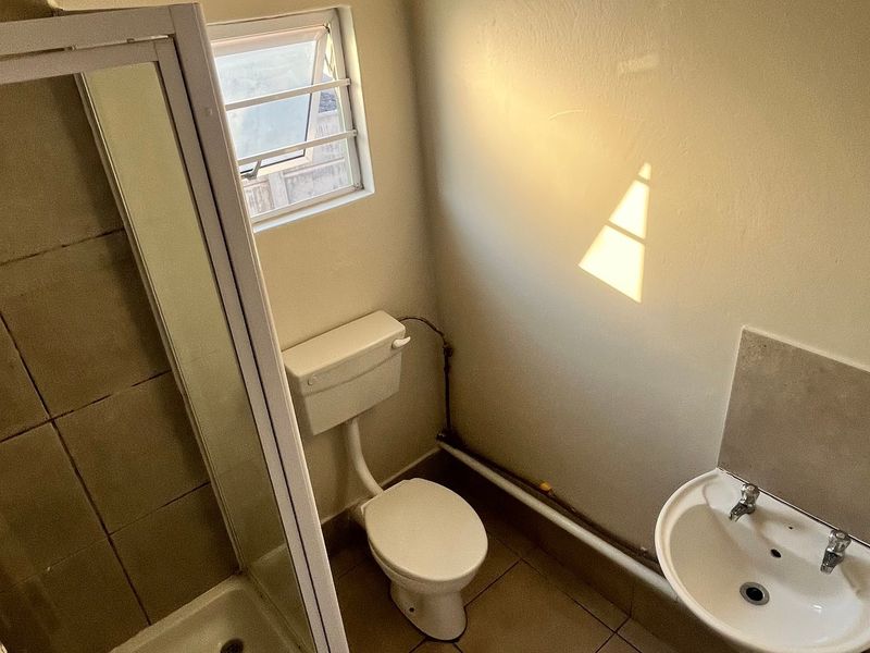 A functional bathroom featuring a shower enclosure, toilet, and wall-mounted basin with tiled flooring and neutral wall finishes.