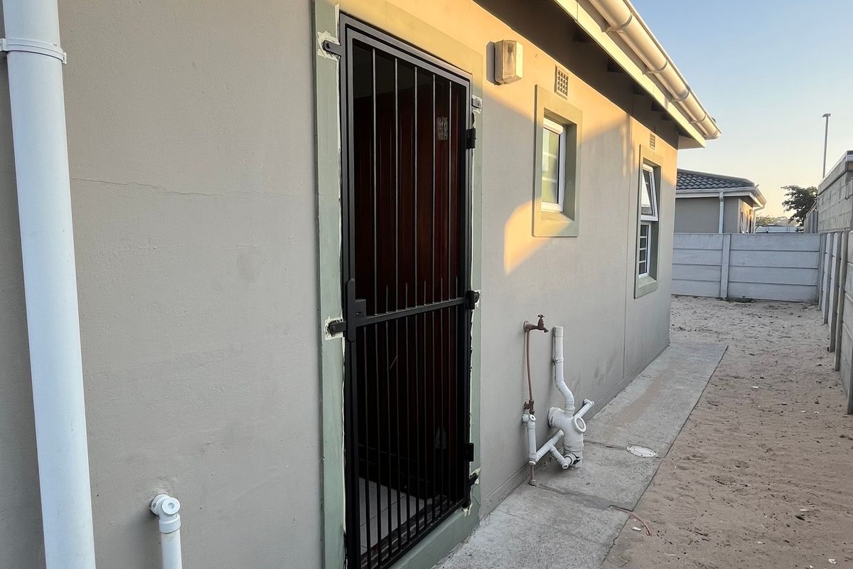 Rear exterior view of the property featuring a security gate, external plumbing fixtures, and a concrete boundary wall.