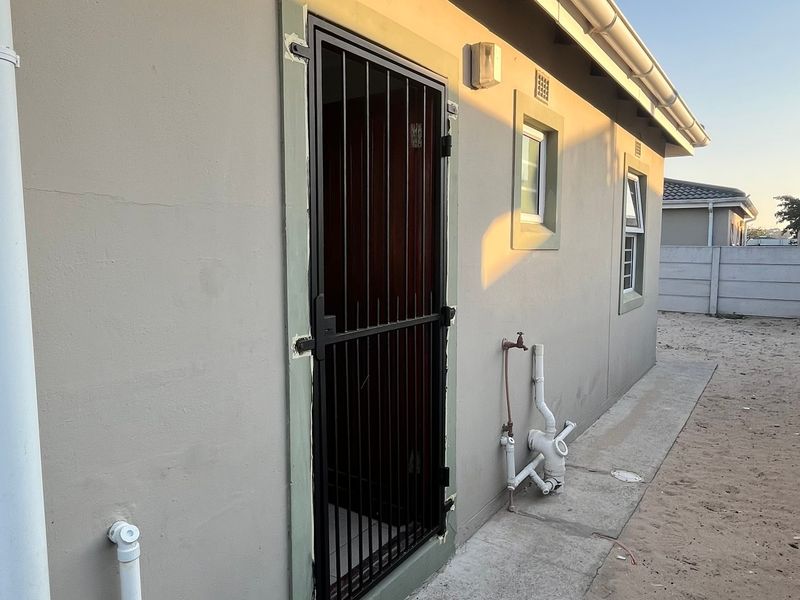 Rear exterior view of the property featuring a security gate, external plumbing fixtures, and a concrete boundary wall.