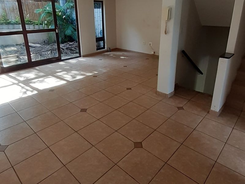An empty, open-plan living area featuring tiled flooring, a staircase with a handrail, and large sliding glass doors leading to an outdoor space.