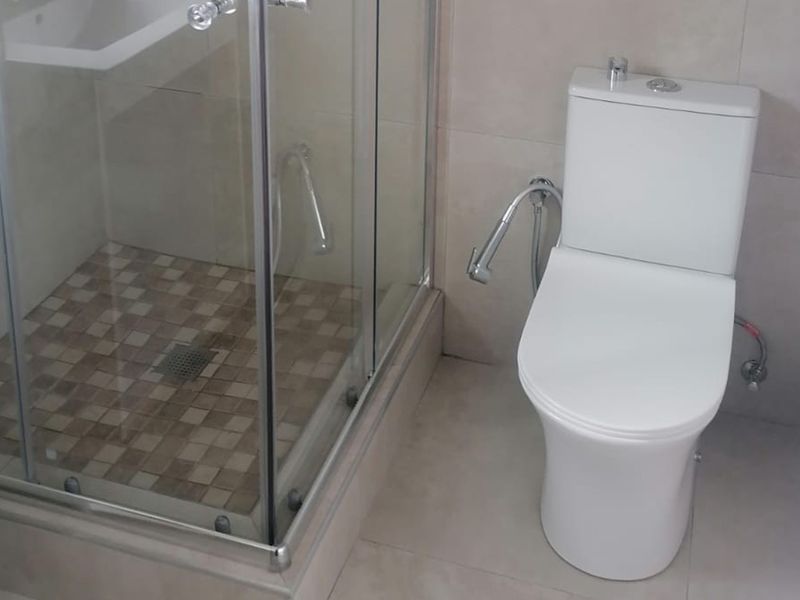 A clean, modern bathroom featuring a glass-enclosed shower with mosaic floor tiles and a contemporary white toilet.