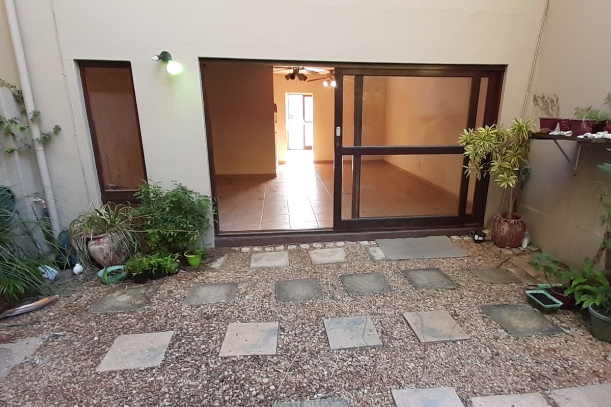 A rear courtyard area featuring a gravel base with paved stepping stones and a large sliding glass door providing access to the interior living space.