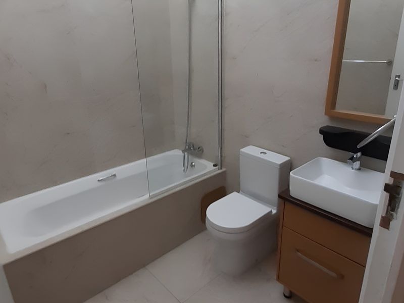 A clean, modern bathroom featuring a bathtub with a glass screen, a contemporary vessel sink vanity, and neutral wall and floor tiling.