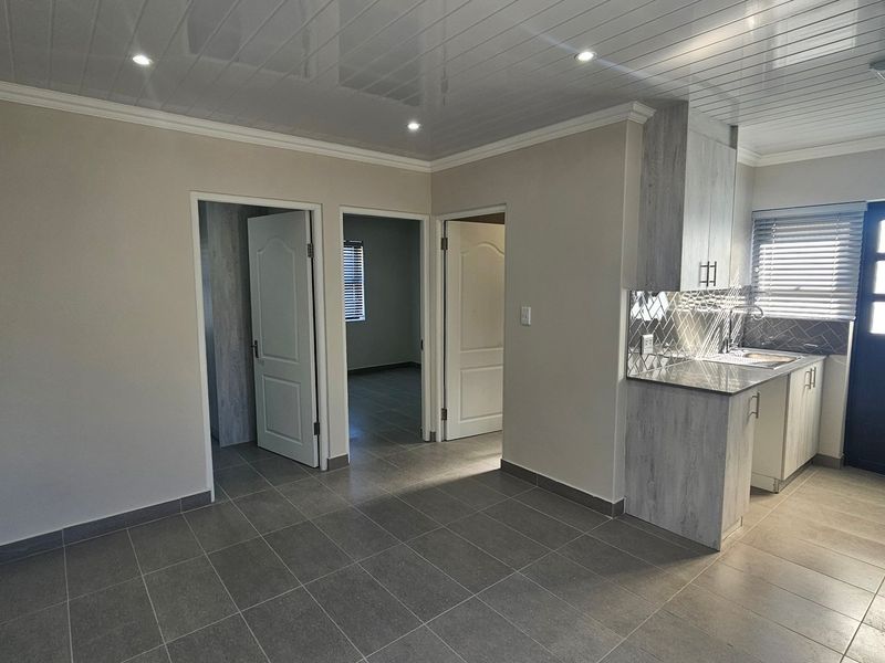 Modern open-plan living area featuring tiled floors, glossy ceiling panels, and a compact kitchen with stone countertops and contemporary finishes.