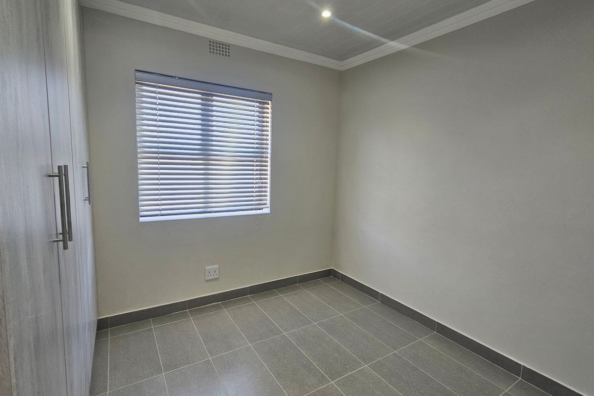 A clean, empty bedroom featuring modern grey tiled flooring, built-in cupboards, and neutral walls, ready for personalization.
