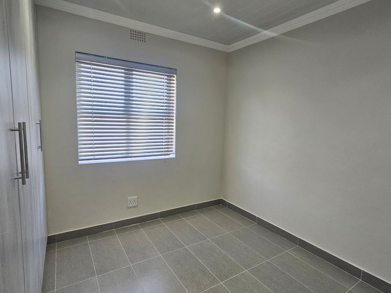 A clean, empty bedroom featuring modern grey tiled flooring, built-in cupboards, and neutral walls, ready for personalization.