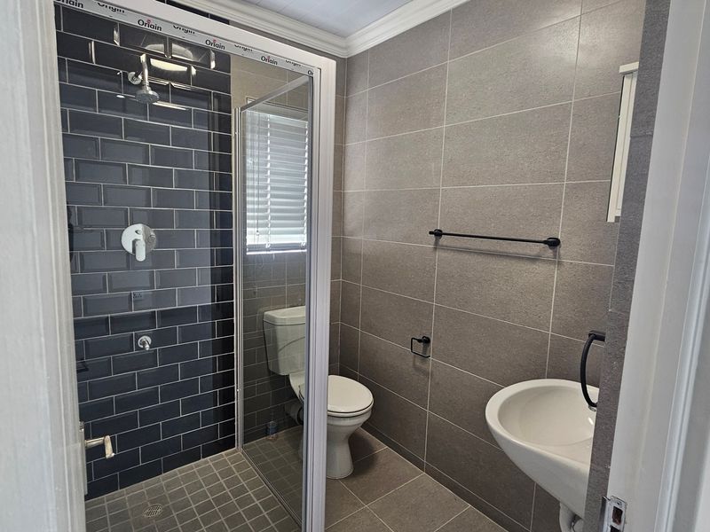 Modern bathroom featuring a walk-in shower with dark subway tiles, neutral wall tiling, a wall-mounted basin, and a toilet.