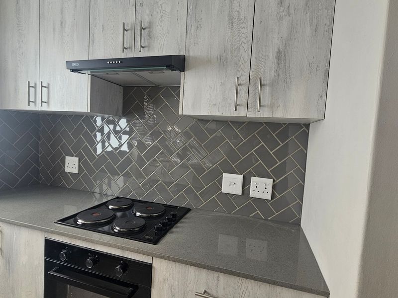 Modern kitchen featuring light wood-grain cabinetry, stone countertops, a sleek electric hob with extractor fan, and a stylish grey herringbone tile backsplash.