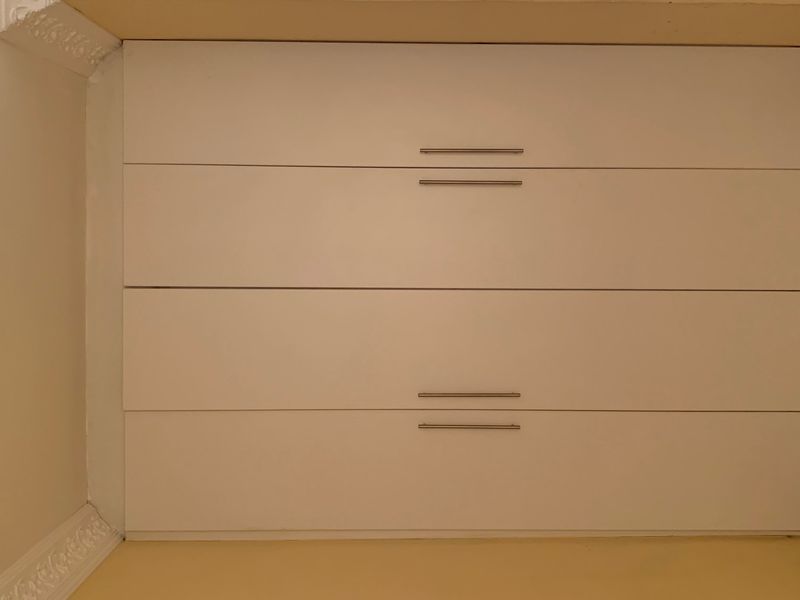 A close-up view of a built-in wardrobe with white cabinetry and modern metal handles, featuring decorative crown molding in the corner.