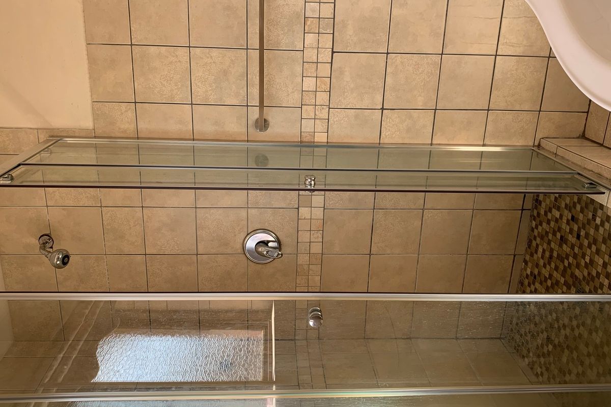 A functional shower area featuring a glass enclosure, tiled walls with mosaic accents, and a standard shower mixer.