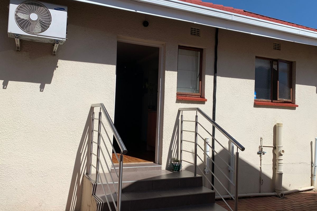 Rear exterior view of the cottage featuring tiled entrance steps with stainless steel handrails and a wall-mounted air conditioning unit.
