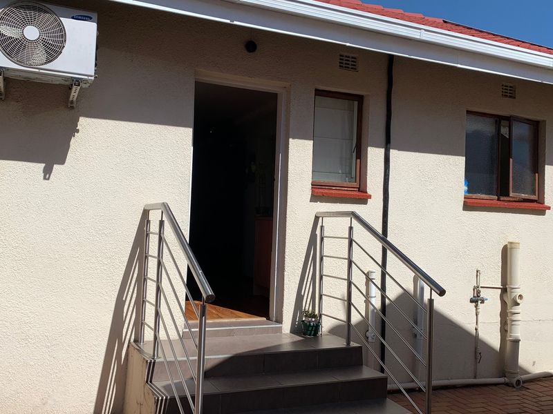 Rear exterior view of the cottage featuring tiled entrance steps with stainless steel handrails and a wall-mounted air conditioning unit.