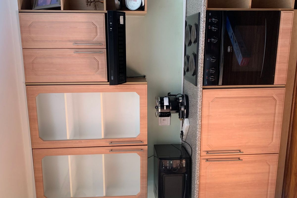 A compact kitchen area featuring wood-finish cabinetry, a built-in oven, and an electric hob set into a laminate countertop.