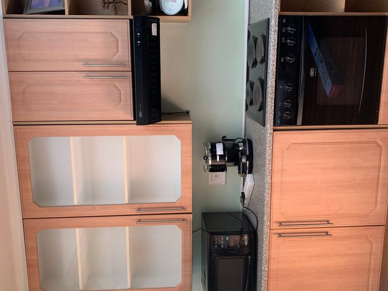 A compact kitchen area featuring wood-finish cabinetry, a built-in oven, and an electric hob set into a laminate countertop.