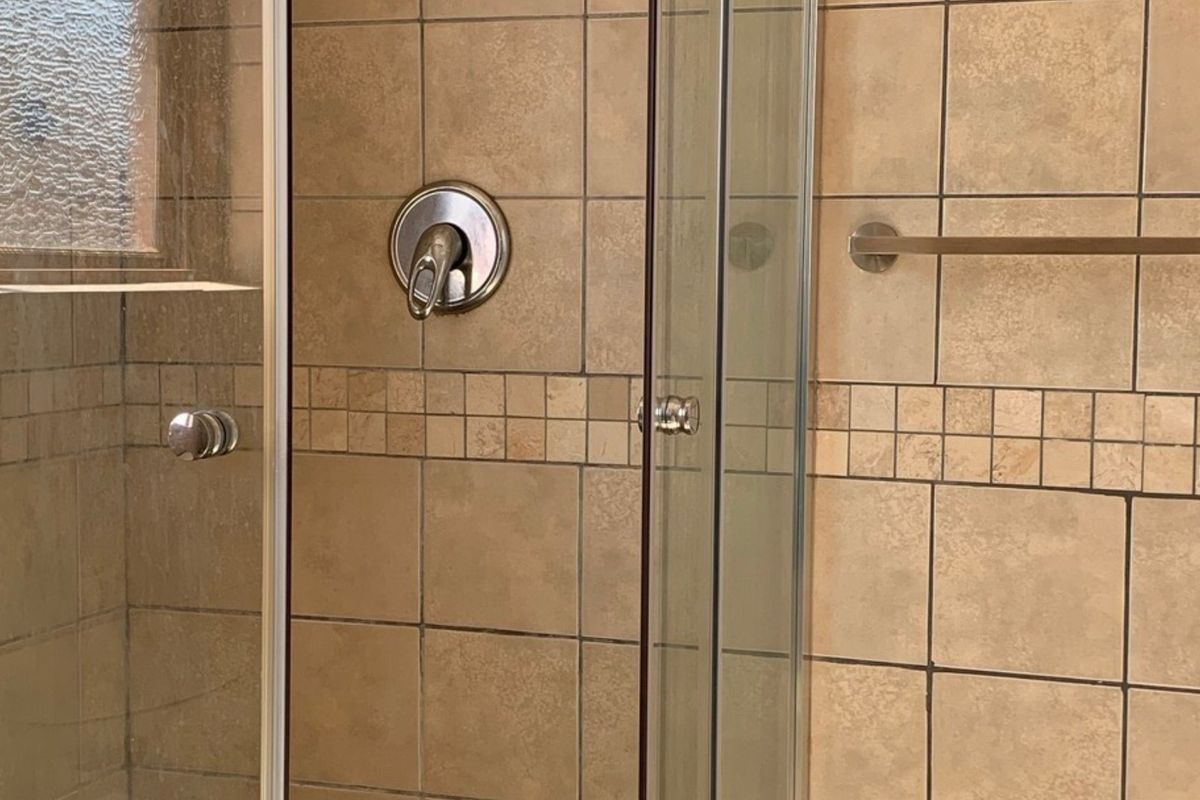 A functional shower enclosure featuring neutral-toned wall tiles, a chrome mixer tap, and a glass door.