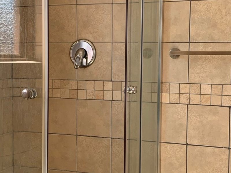 A functional shower enclosure featuring neutral-toned wall tiles, a chrome mixer tap, and a glass door.