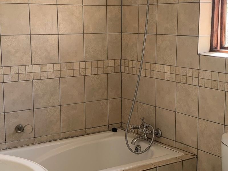 A functional bathroom featuring a built-in bathtub with a shower mixer, tiled walls, and a standard toilet.