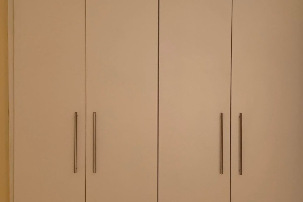 A bedroom featuring clean, white built-in cupboards with modern metal handles, providing ample storage space.