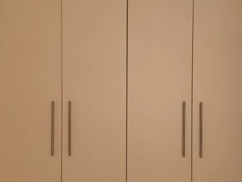 A bedroom featuring clean, white built-in cupboards with modern metal handles, providing ample storage space.