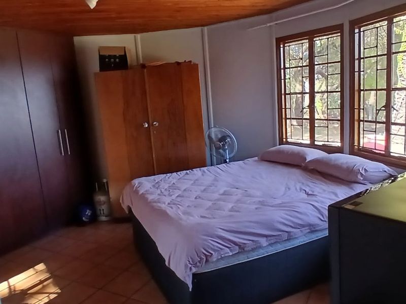 A bedroom featuring tiled flooring, a wooden ceiling, and built-in cupboards, with large windows fitted with security bars.
