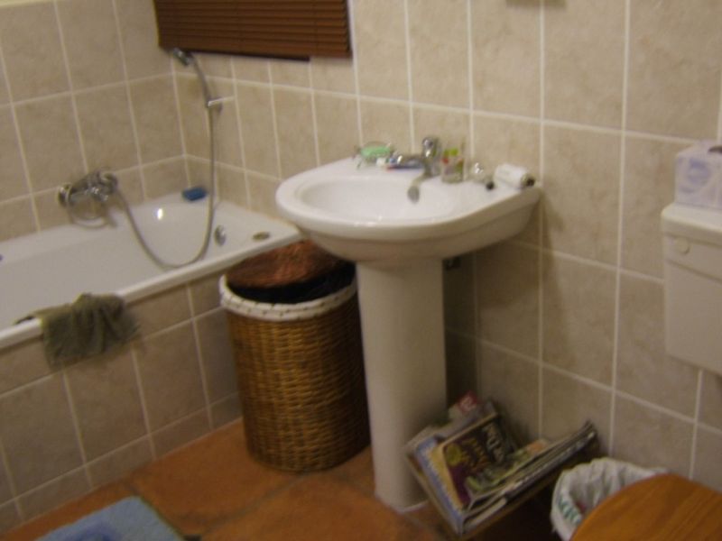 A functional bathroom featuring a pedestal basin, bathtub with shower mixer, and neutral ceramic wall and floor tiling.
