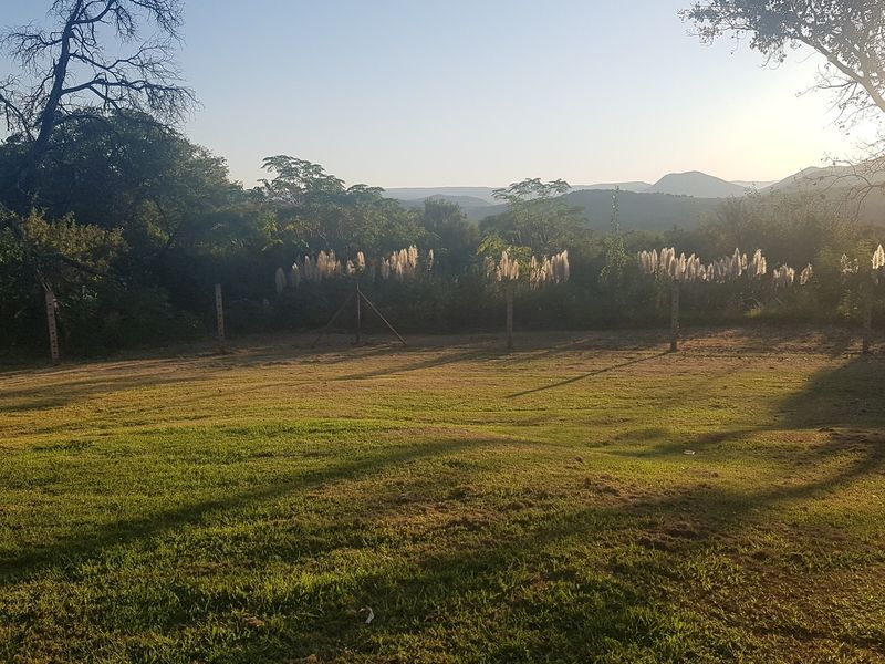 A spacious, open garden area featuring a well-maintained lawn and perimeter fencing, set against a scenic natural landscape backdrop.