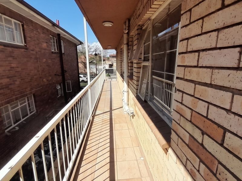 A narrow exterior balcony featuring tiled flooring, a metal safety balustrade, and facebrick wall finishes, providing access to the apartment's windows.