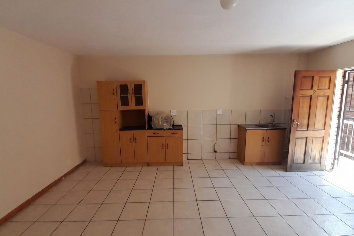 An empty kitchen area featuring tiled flooring, tiled splashbacks, and basic built-in wooden cabinetry with a sink.