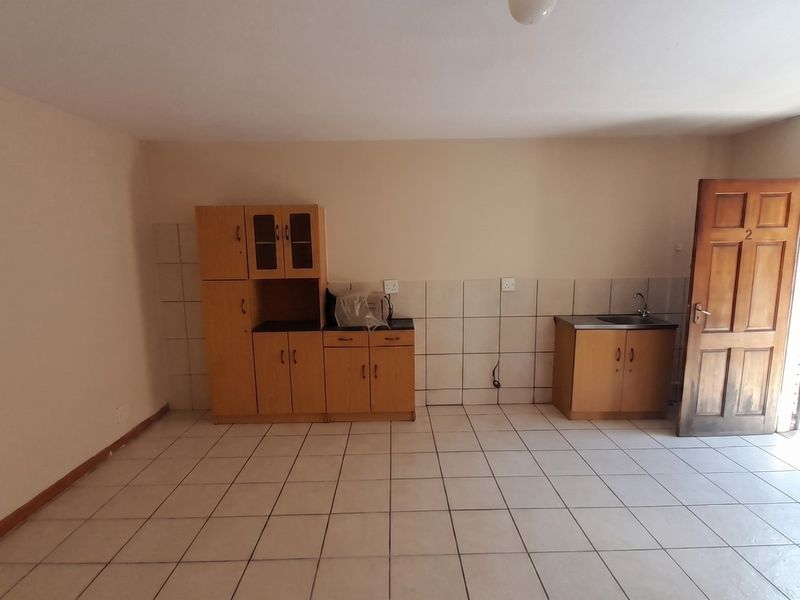 An empty kitchen area featuring tiled flooring, tiled splashbacks, and basic built-in wooden cabinetry with a sink.