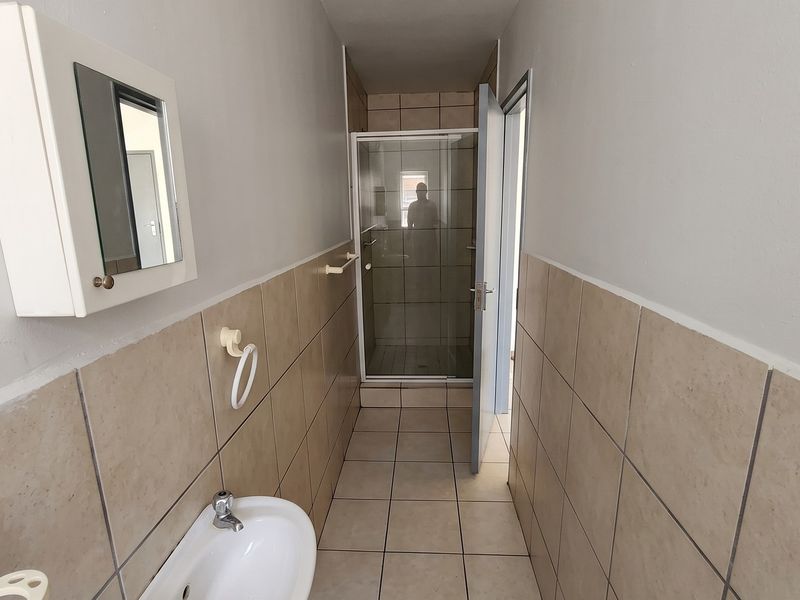 A functional bathroom featuring a shower enclosure, pedestal basin, and wall-mounted medicine cabinet with neutral tiled finishes.