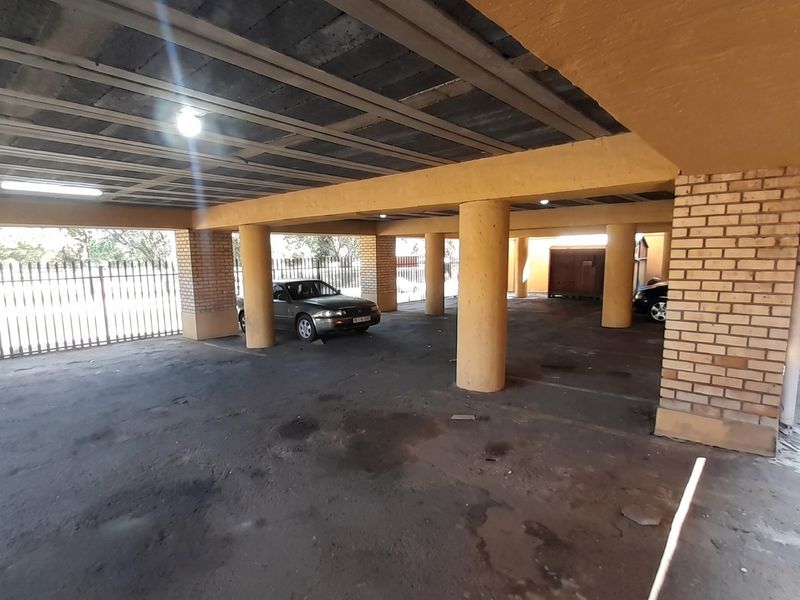 A covered parking area featuring concrete columns, exposed ceiling structure, and brick pillars, providing secure off-street parking for the property.