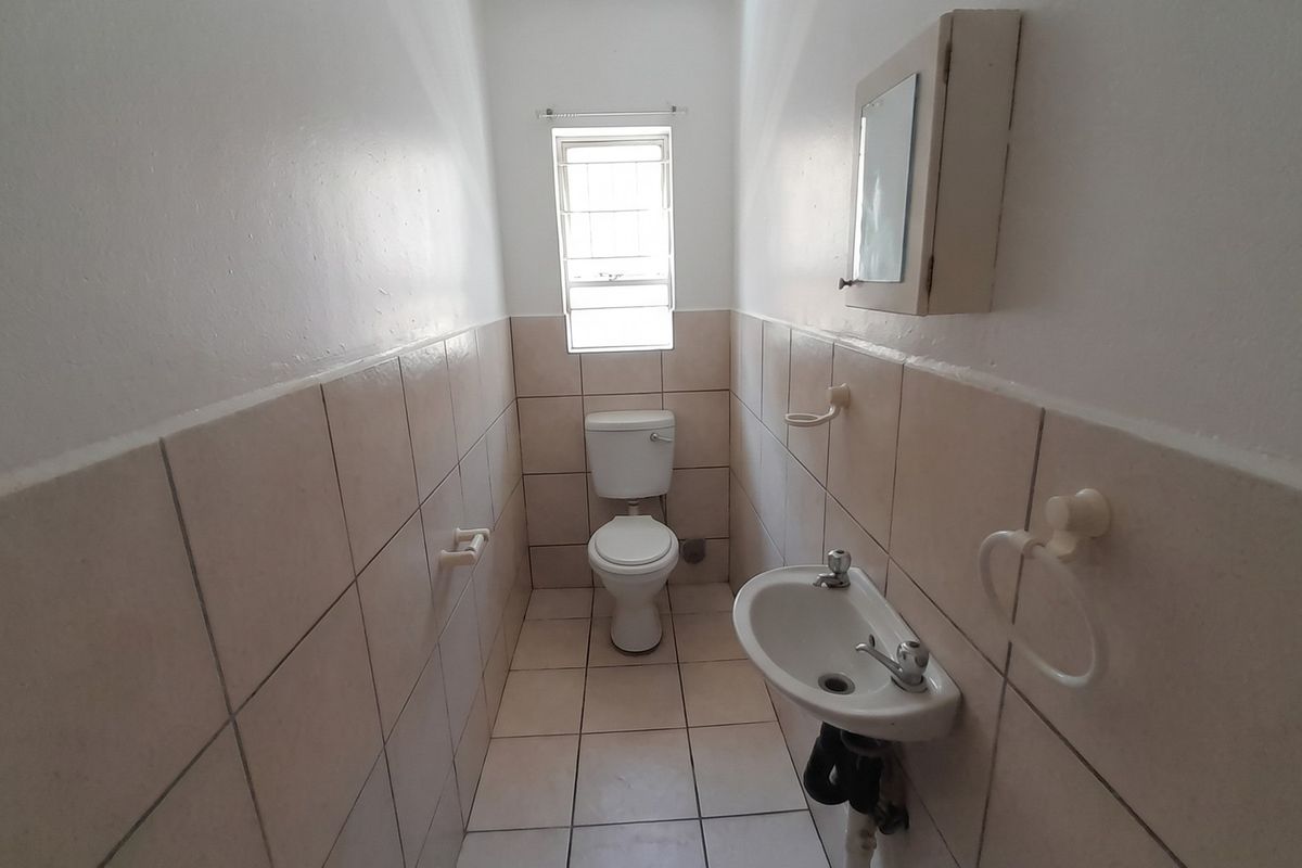 A compact guest bathroom featuring tiled walls and flooring, a standard toilet, and a wall-mounted basin with an integrated medicine cabinet.