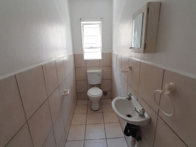 A compact guest bathroom featuring tiled walls and flooring, a standard toilet, and a wall-mounted basin with an integrated medicine cabinet.