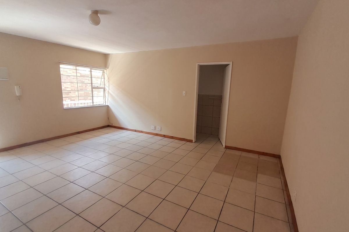 A spacious, empty living area featuring neutral tiled flooring, a window with security bars, and an intercom system, ready for personalization.