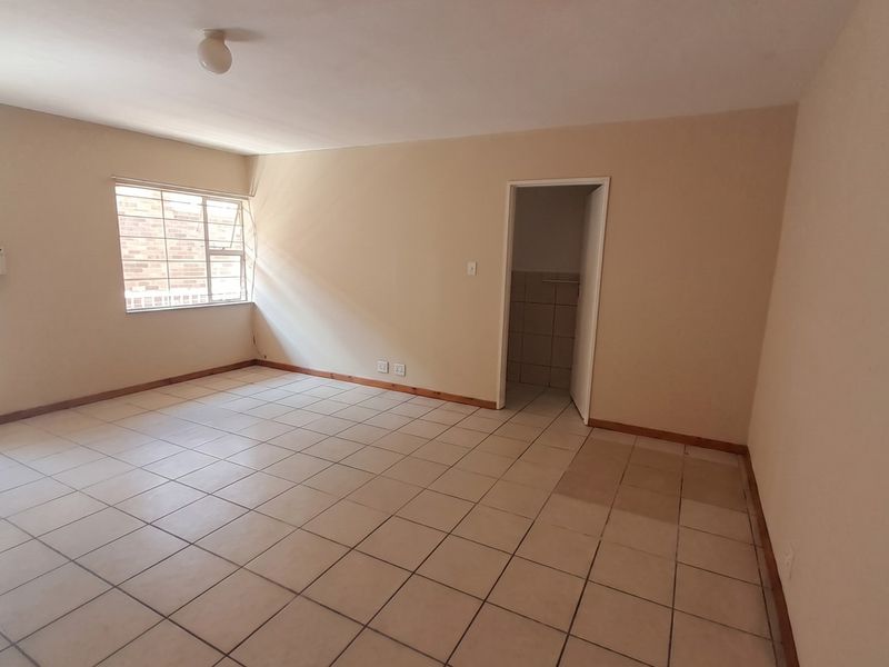 A spacious, empty living area featuring neutral tiled flooring, a window with security bars, and an intercom system, ready for personalization.