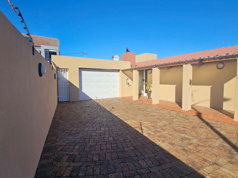 Front exterior view featuring a paved driveway, covered walkway, and secure garage access with perimeter electric fencing.