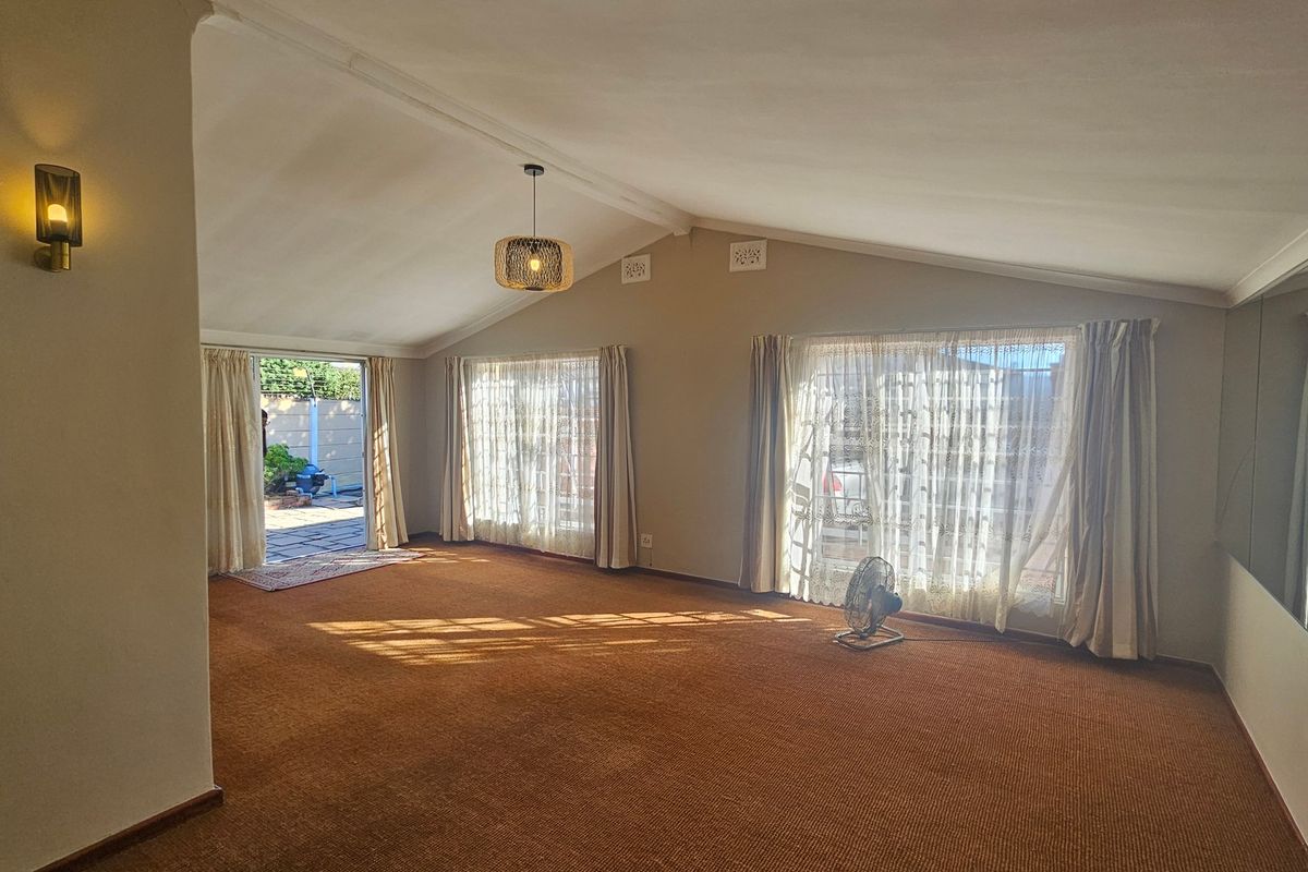 Spacious living room featuring a vaulted ceiling, large windows for natural light, and direct access to an outdoor patio area.