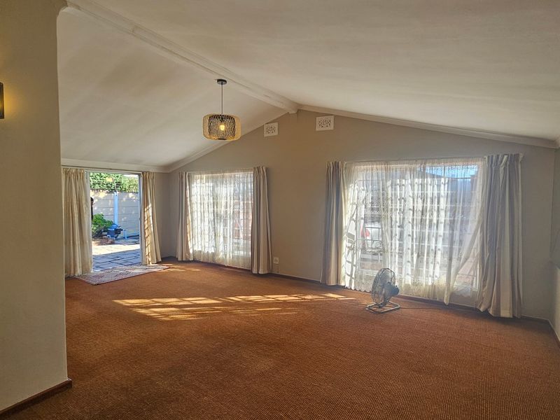 Spacious living room featuring a vaulted ceiling, large windows for natural light, and direct access to an outdoor patio area.