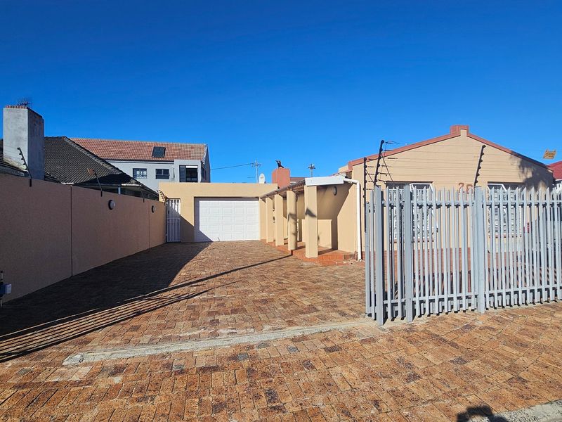 Front exterior view of the property featuring a paved driveway, secure boundary wall with electric fencing, and a private garage entrance.