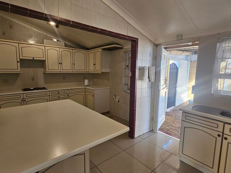 A dated kitchen featuring built-in cabinetry, tiled splashbacks, and a double bowl sink, with direct access to an exterior paved area.