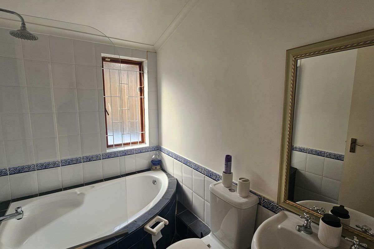 A functional bathroom featuring a corner bathtub with shower attachment, pedestal basin, and wall-mounted mirror, finished with classic tiled splashbacks.